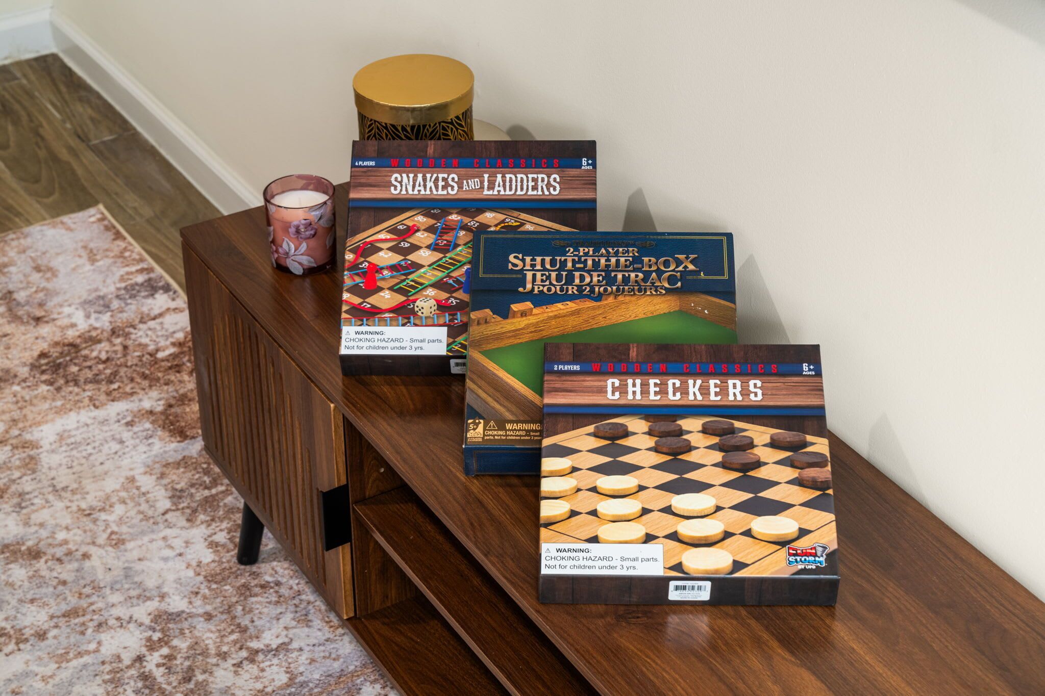 Una mesa de madera con tres juegos de mesa: 'Snakes and Ladders', 'Shut the Box' y 'Checkers'.