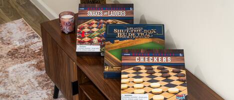 Una mesa de madera con tres juegos de mesa: 'Snakes and Ladders', 'Shut the Box' y 'Checkers'.