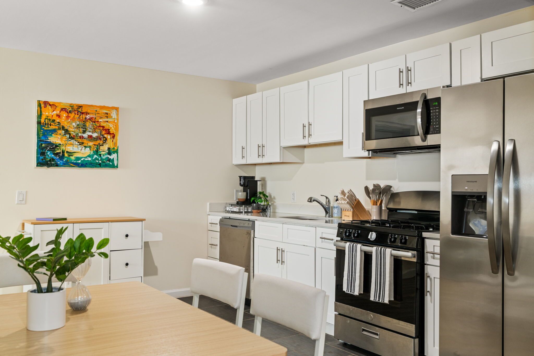 Een moderne keuken met witte kastjes, roestvrijstalen apparatuur, een magnetron, oven en een eethoek met een tafel en stoelen.