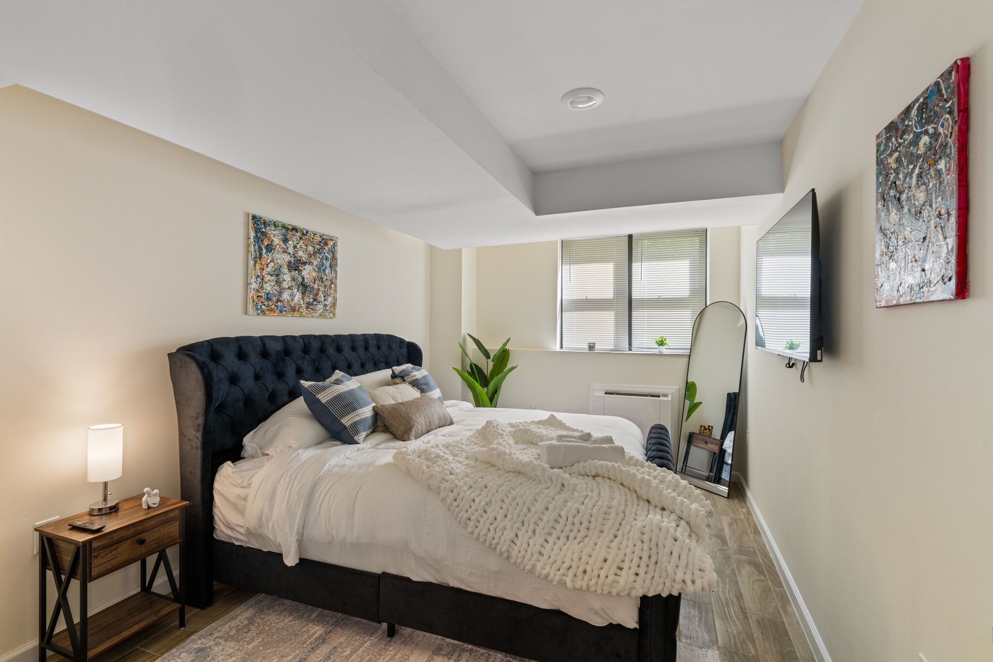 A bedroom with a bed, bedside table, lamp, and artwork.