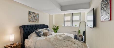 A bedroom with a bed, bedside table, lamp, and artwork.