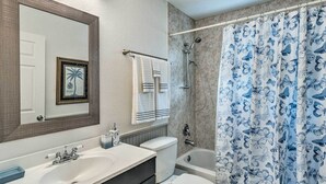 A bathroom with a sink, toilet, bathtub, and shower curtain. - Stylish Coastal  Cottage Near Downtown Punta Gorda (Punta Gorda)