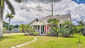 A single-story house with a front porch, a red door, and a small garden with palm trees. - Stylish Coastal  Cottage Near Downtown Punta Gorda (Punta Gorda)