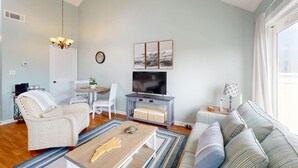 A living room with a sofa, a chair, a coffee table, a TV, and a small table with a lamp. - Flippers Pad at Pebble Beach | Pool View·EI Studio (Emerald Isle)