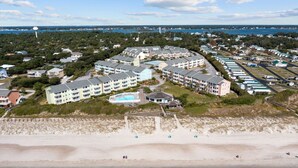 A coastal hotel with multiple buildings, a beach, and a water tower. - Flippers Pad at Pebble Beach | Pool View·EI Studio (Emerald Isle)
