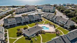 A coastal hotel complex with multiple buildings, a central pool, and a view of the ocean. - Flippers Pad at Pebble Beach | Pool View·EI Studio (Emerald Isle)