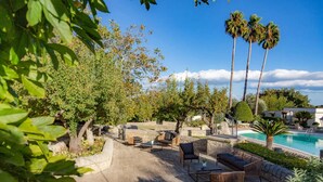 A poolside area with lounge chairs, a stone wall, and palm trees. - Relais Villa Caia (Noto)