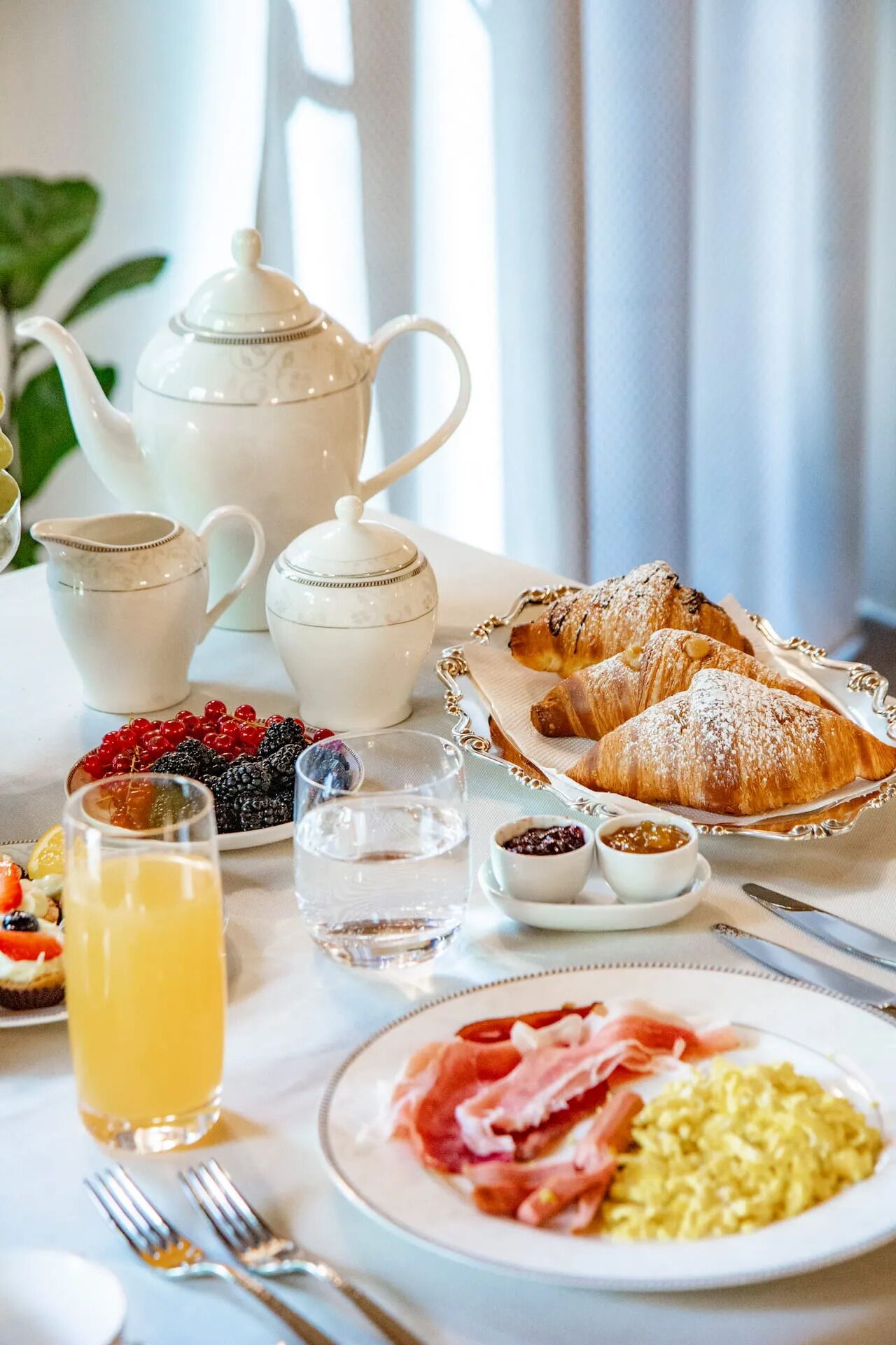 A breakfast setting with croissants, fruit, and a teapot.