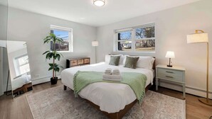 Un dormitorio moderno con una cama grande, lámparas de noche, una planta en maceta y vistas al exterior.