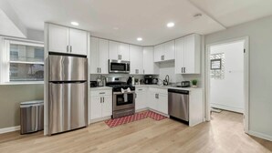 Una cocina moderna con armarios blancos, electrodomésticos de acero inoxidable y un tapete rojo estampado.