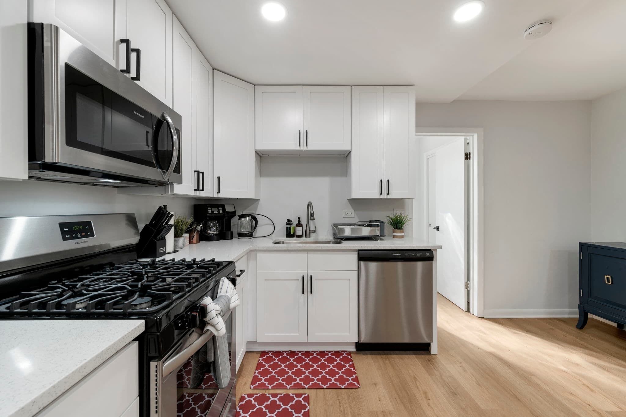 A modern kitchen with white cabinets, stainless steel appliances, and a wooden floor.