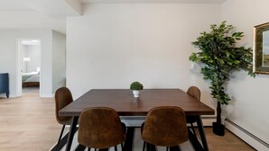 Un comedor con una mesa de madera, cuatro sillas, una planta pequeña en maceta y una planta grande en maceta.