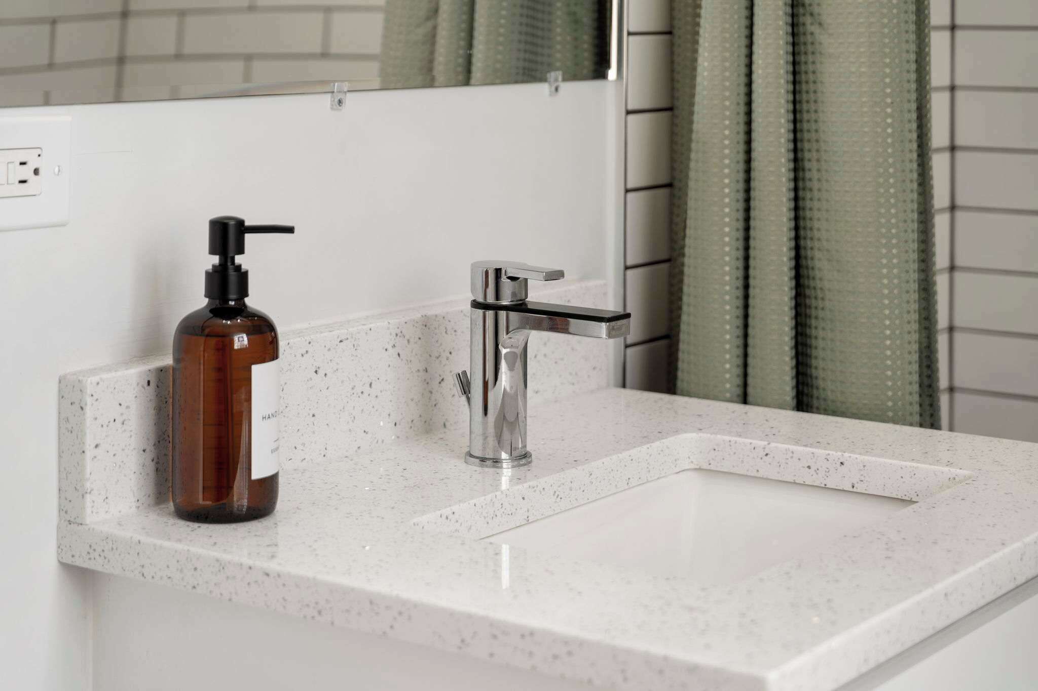 Une salle de bain avec un comptoir blanc à motifs, un robinet chromé et un distributeur de savon marron.