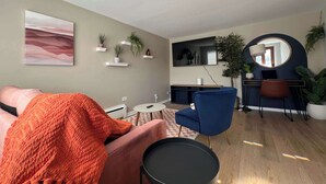 A modern living room with a sofa, a coffee table, and a TV. There are plants on shelves and a round mirror on the wall.