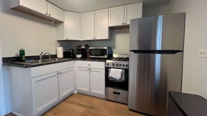 A modern kitchen with white cabinets, a stainless steel refrigerator, a microwave, a stove, and a sink.