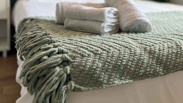 A neatly made bed with a green headboard, a folded white towel, and a textured throw blanket.