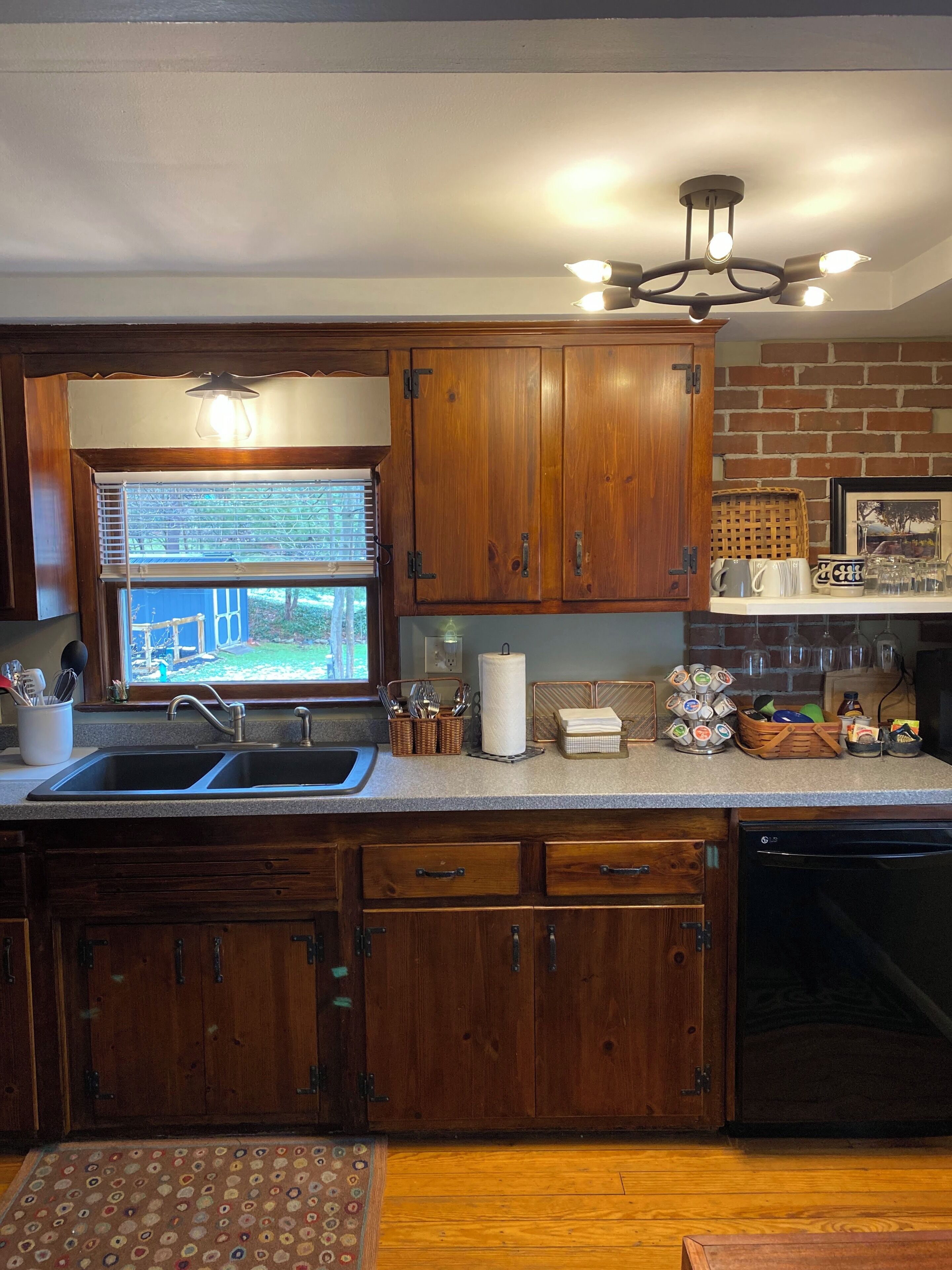 A kitchen with wooden cabinets, a double sink, a dishwasher, and a window with blinds.