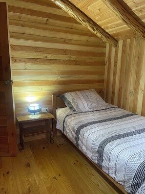 Ein Schlafzimmer in einer Holzhütte mit einem Bett, einem Nachttisch und einer Wandlampe.