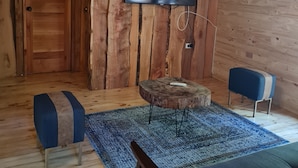 Ein Zimmer mit Holzboden, an der Wand ein Fernseher, ein runder Holztisch, ein blaues Sofa und eine Bank.
