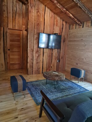 Ein Zimmer mit Holzboden, an der Wand ein Fernseher, ein runder Holztisch, ein blaues Sofa und eine Bank.