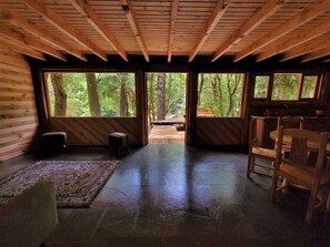Ein Blockhauskamin mit Steinfußboden, Holzwänden und großen Fenstern mit Blick auf einen Wald.