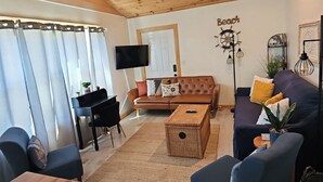 Una sala de estar con un sofá marrón, un sofá azul, un televisor, un escritorio y una pared con un cartel que dice 'Beach'.