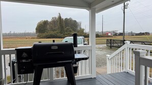 Un porche cubierto con una parrilla, vista a un campo y un vehículo distante.