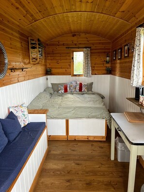 Interior acogedor de una cabaña con una cama, un sofá, una mesa y un ventanal.