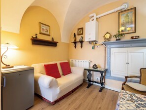 A room with a white sofa, a small refrigerator, a radiator, a fireplace, and a table with a lamp. - La Quiete by Interhome (Verbania)