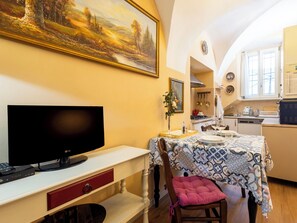 A dining area with a table set for two, a television on a stand, and a painting above the table. - La Quiete by Interhome (Verbania)