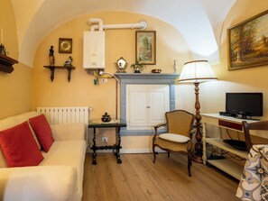 Une pièce chaleureuse avec un canapé blanc, une chaise en bois, une petite table avec une lampe, un téléviseur et une cheminée.