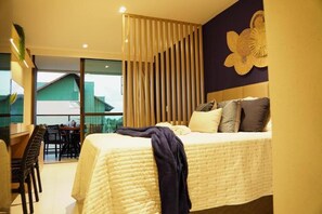 Ein Schlafzimmer mit Bett, Schreibtisch und Blick auf ein grünes Gebäude vor der Tür.