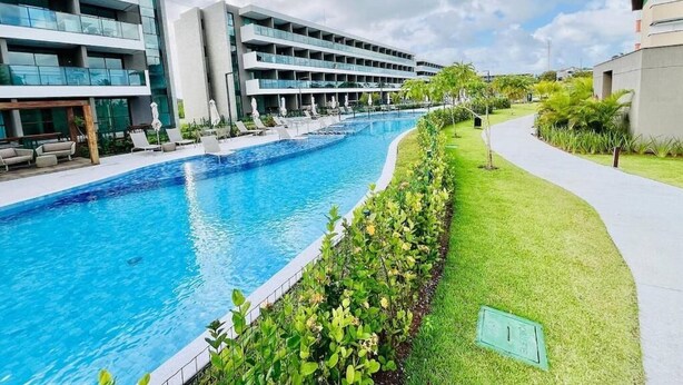 Un hotel moderno con piscina, numerosi balconi e un prato curato.