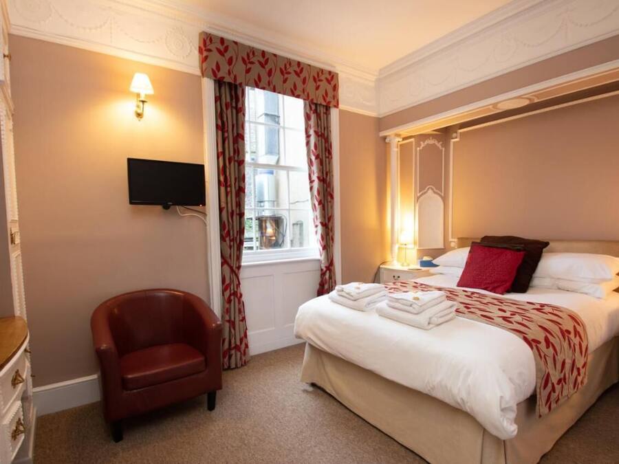 A hotel room with a bed, a chair, a TV, and a window with curtains.