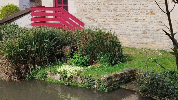 A stone building with a red door and shutters, a small bridge, and a waterway. - House by the river, 12 kms from the sea, shops, 10 km from Caen (Cairon)