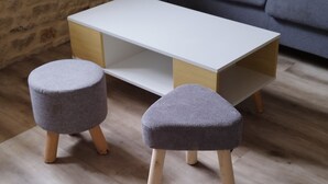 A room with a wooden floor, a white table, two grey ottomans, and a dark sofa. - House by the river, 12 kms from the sea, shops, 10 km from Caen (Cairon)