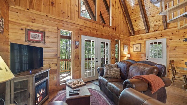 A log cabin interior with a fireplace, leather sofa, television, and wooden walls. - Quiet Retreat for Couples, Wi-Fi, Coz,y, Great Location (Rogers)