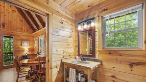 A wooden cabin interior with a dining area, a sink with a mirror, and a window with a view of greenery. - Quiet Retreat for Couples, Wi-Fi, Coz,y, Great Location (Rogers)