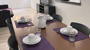 Un comedor con una mesa lista para dos personas, una cafetera y un refrigerador al fondo.