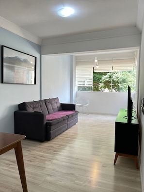 Una sala de estar con sofá, mueble para televisión, mesa de comedor y ventana con persianas.