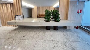 Un área de recepción con un mostrador alargado, un sofá de cuero y plantas en macetas.