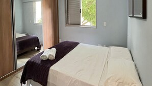 Un dormitorio con cama, espejo, ventana y lámpara en el techo.