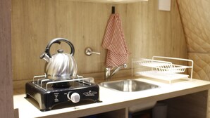 A compact kitchen with a kettle, sink, and storage shelves.