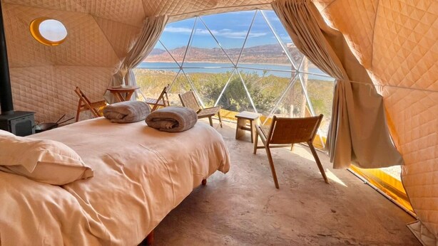 A cozy tented room with a bed, chairs, and a view of the landscape.