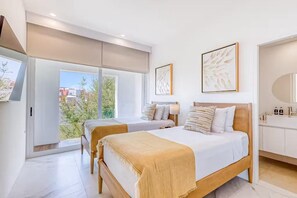 Un dormitori modern amb dos llits, una finestra gran i un bany amb mirall i productes de tocador.