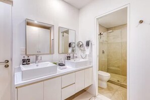 Un bany modern amb un doble lavabo, un vàter i una dutxa amb envàs de vidre.