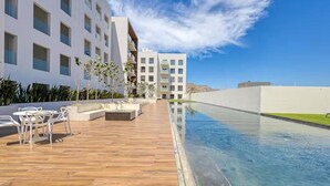Ein modernes Hotel mit Pool, Sitzgelegenheiten im Freien und blauem Himmel.
