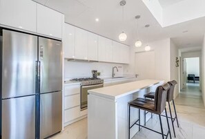 A modern kitchen with stainless steel appliances, white cabinetry, and a central island with bar stools. - Stylish 3BR Downtown Cabo Condo, Walk Everywhere! (Cabo San Lucas)