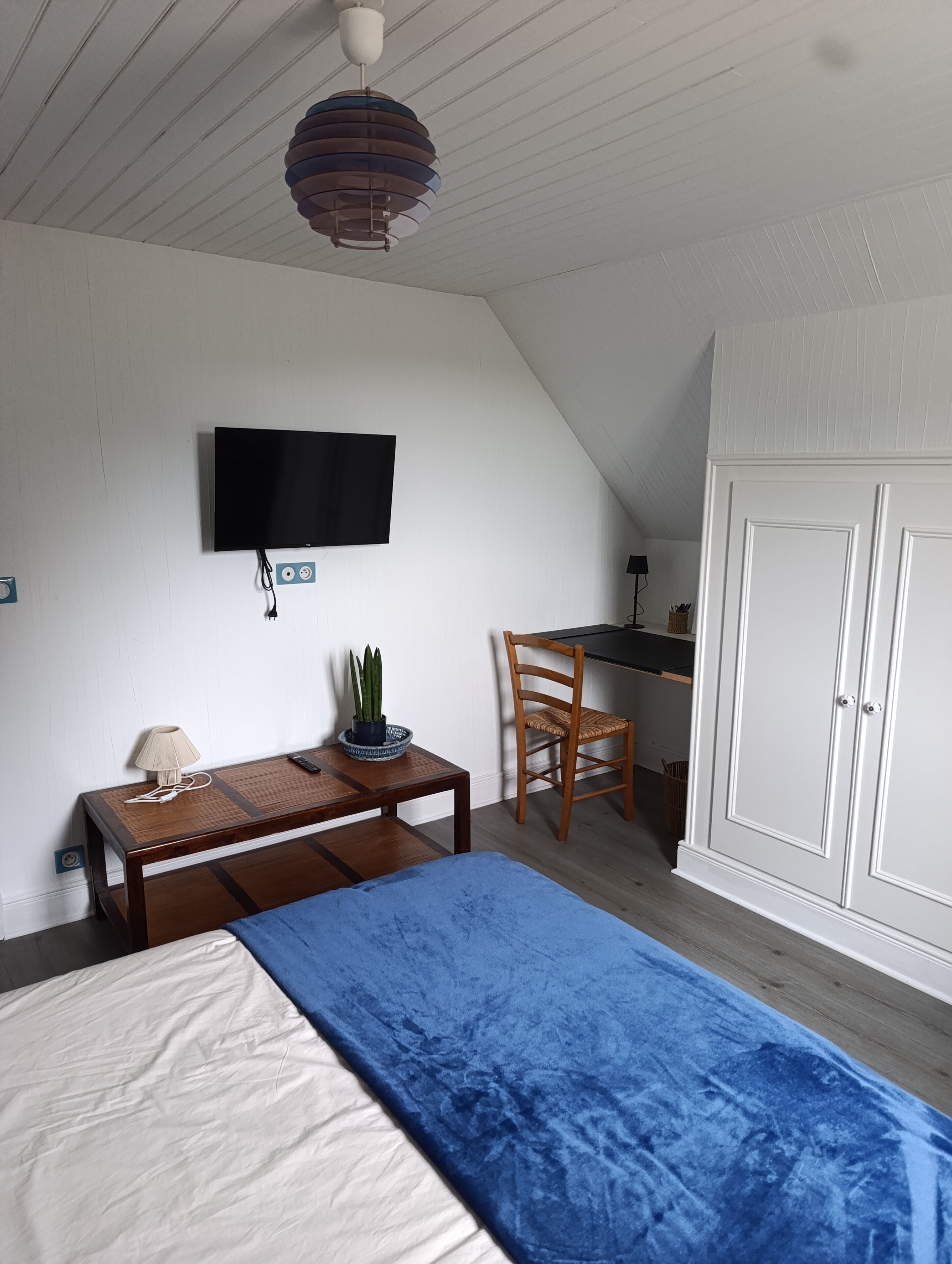 A bedroom with a bed, a desk, a chair, a television, and a wardrobe.