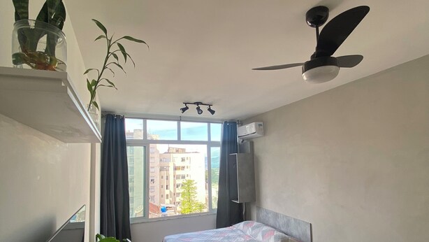 Ein Schlafzimmer mit Bett, Sofa, Deckenventilator, Fenster mit Vorhängen und einer Topfpflanze.